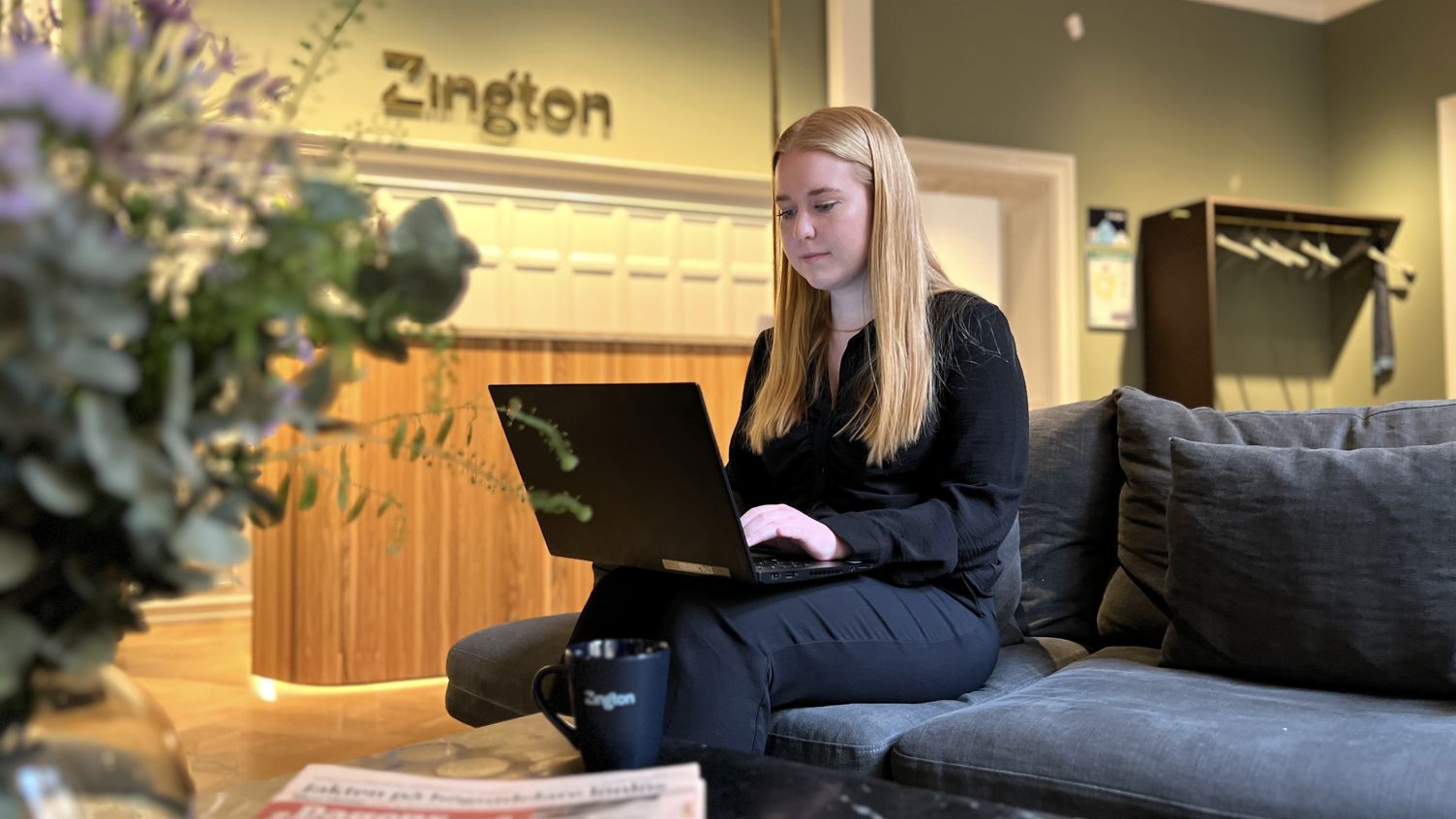 Zingtons medarbetare Melanie sitter i en soffa i företagets gröna lobby, engagerad i sitt arbete på en laptop i hennes famn.
